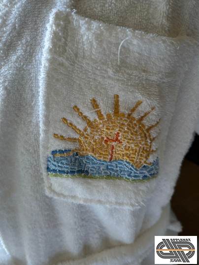 Broderie sur textile style serviette éponge qui montre un soleil sur ce qui semble être de l'eau en mouvement